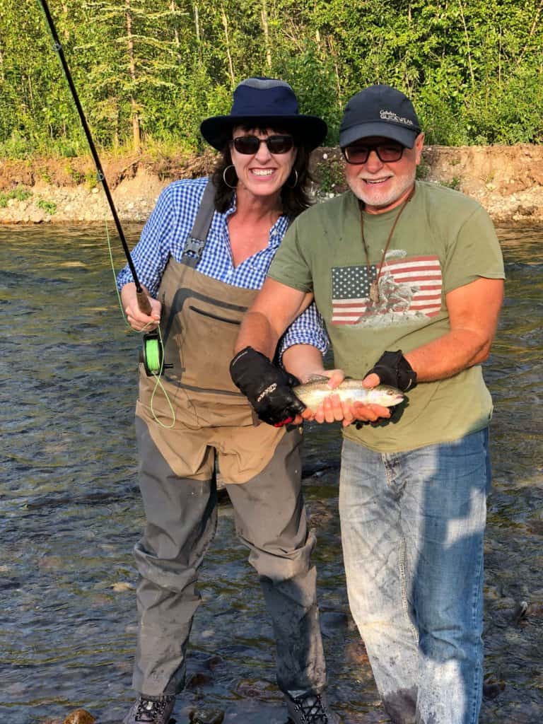 Man and lady standing in a shallow river holding a fish