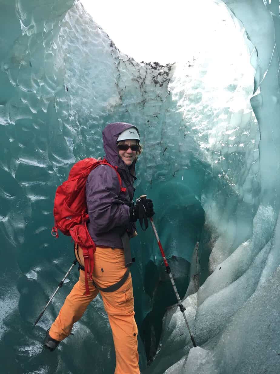 female standing inside blue ice holding poles and wearing a backpack