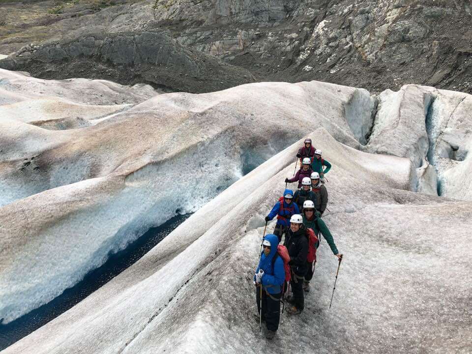 9 people standing on a glacier at the top of a crevasse