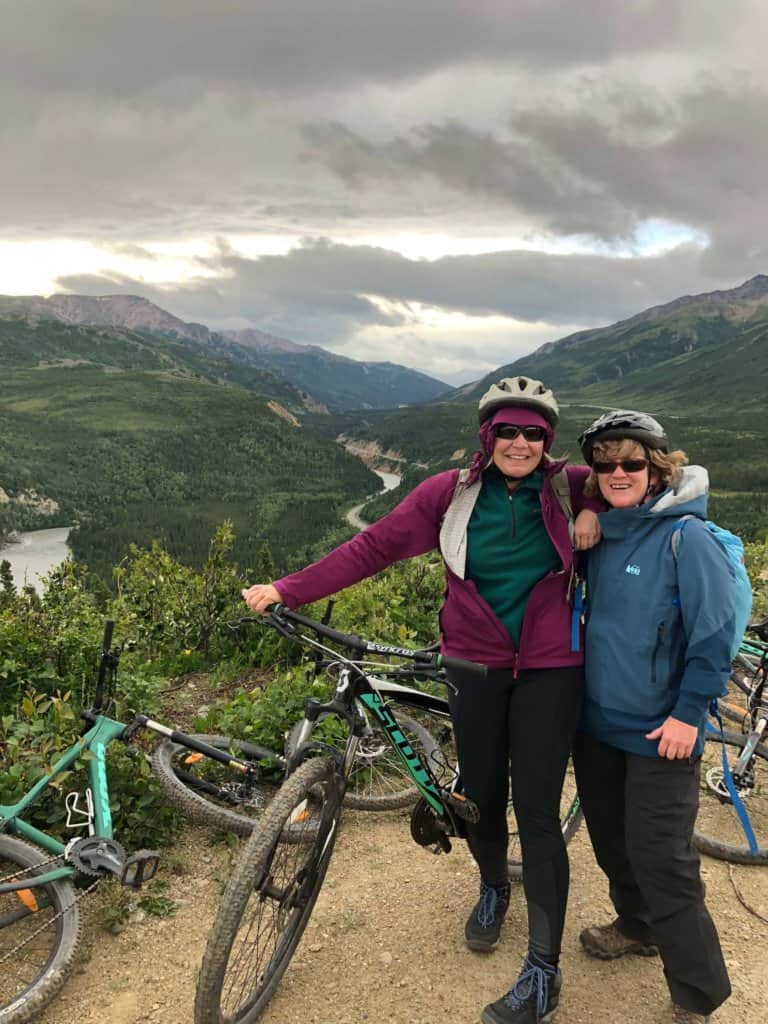 2 female friends with bicycles on top of a mountain