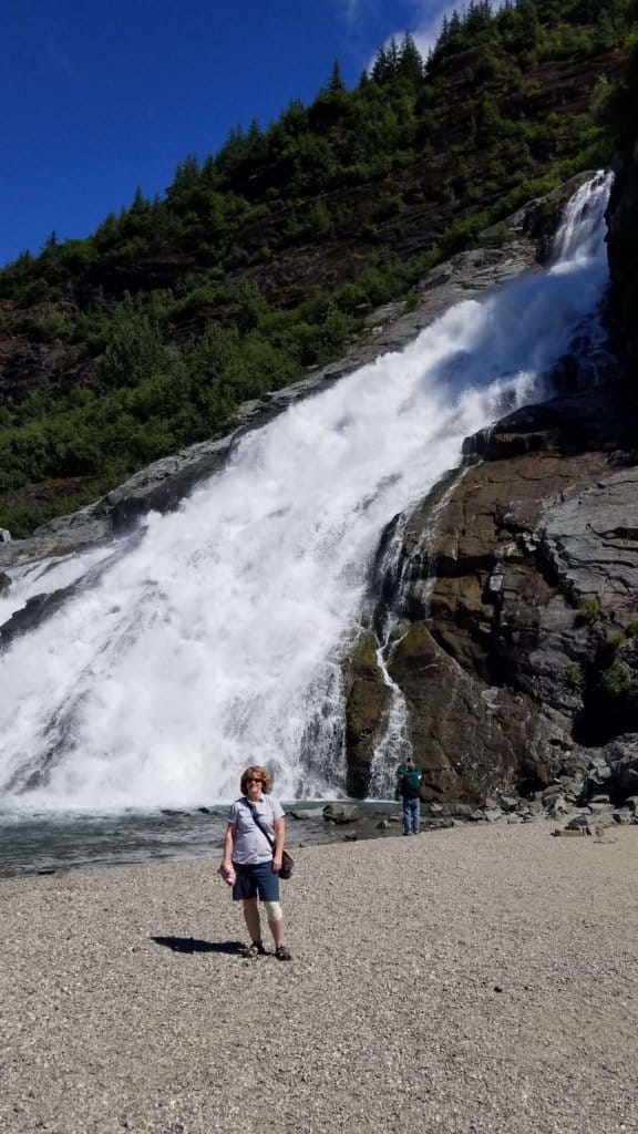 a female standing on the beach with a waterfall behind her