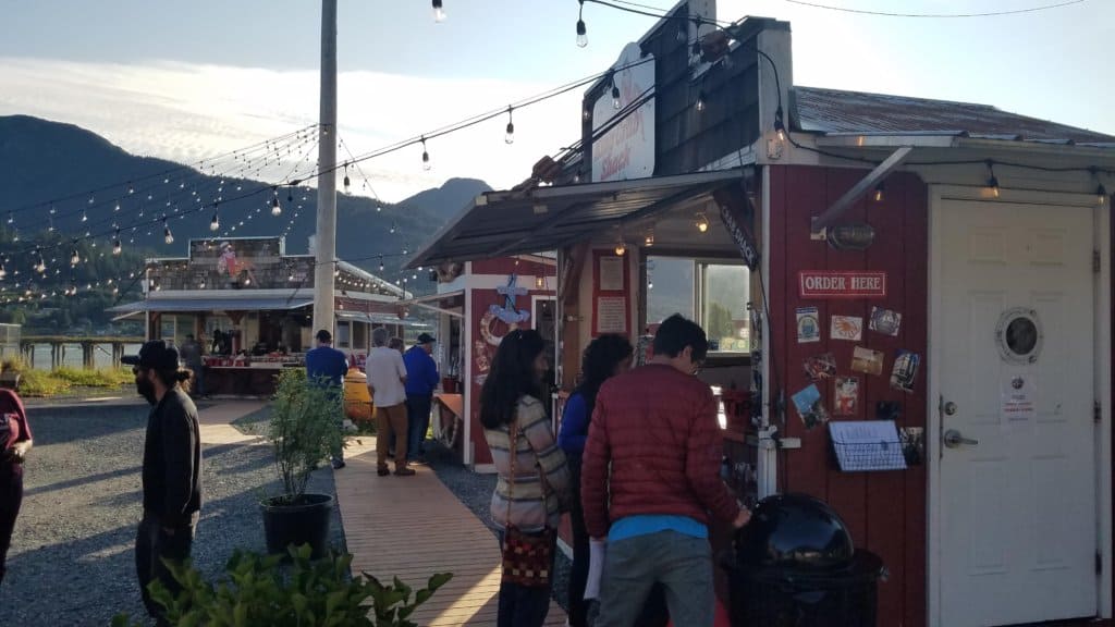 3 small red buildings outside each with people standing in front