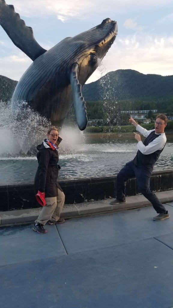 male and female standing in front of a statue of whale breaching