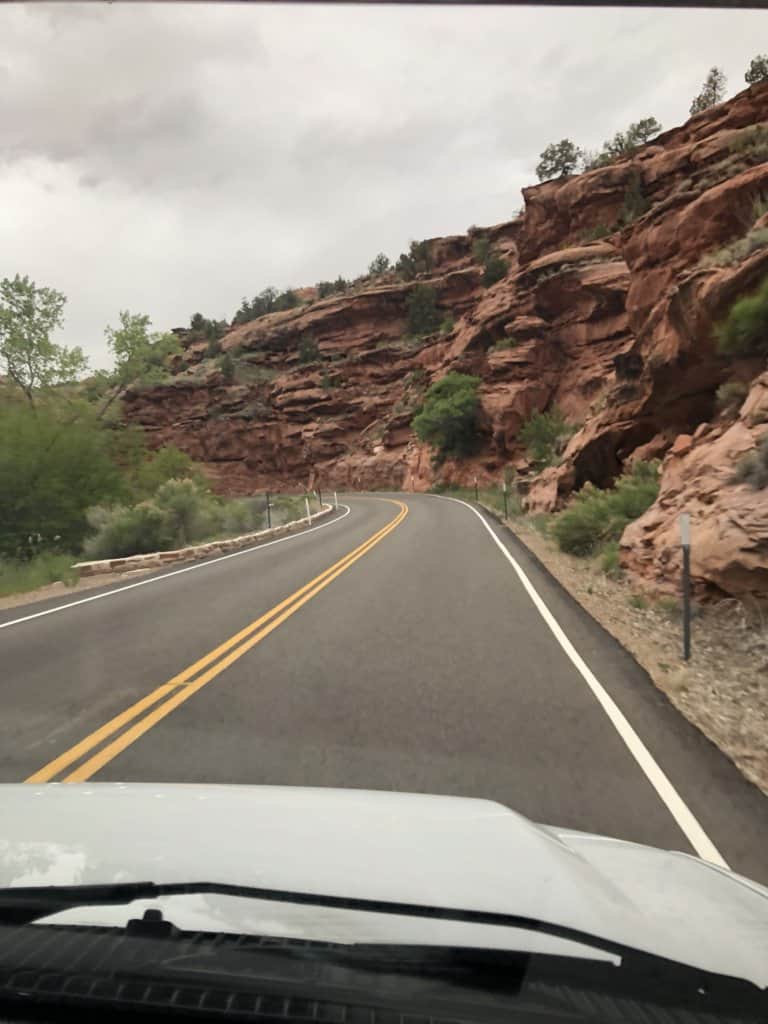 from passenger seat in a vehicle going down the road with red rocks on the side