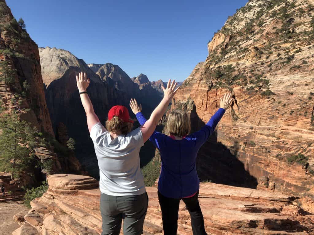 2 females from behind with hands in air high above a canyon