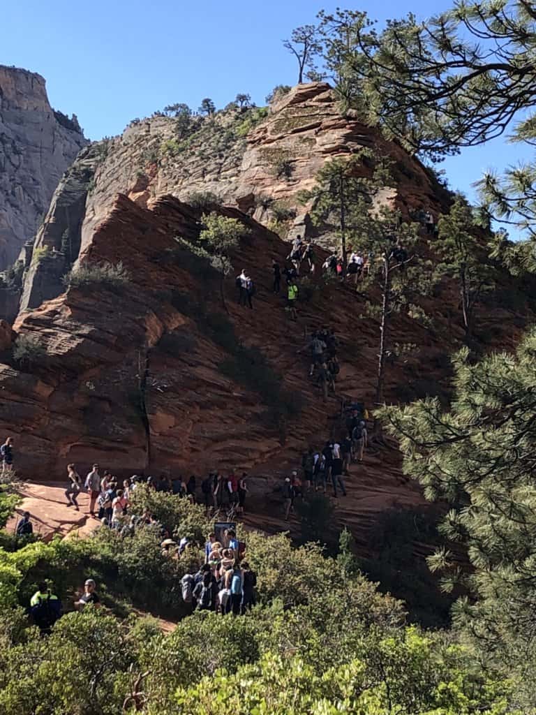 a line of people waiting on a hike trail going up
