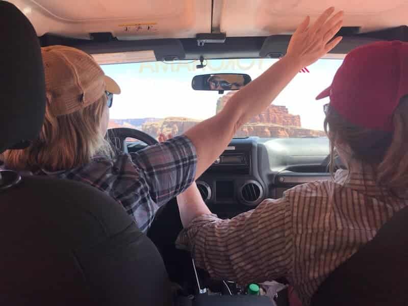 2 women inside a Jeep with hands in the air