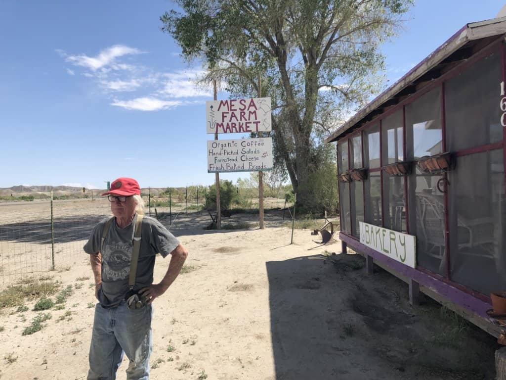 man standing in front of building with sign reading Mesa Farm Market