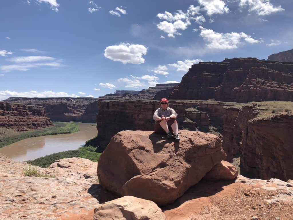 female sitting on a rock in the desert high above a river